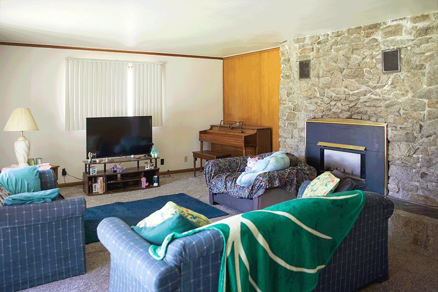 A side view of a cozy living room with three sofas, a TV, a piano and a stone fireplace.